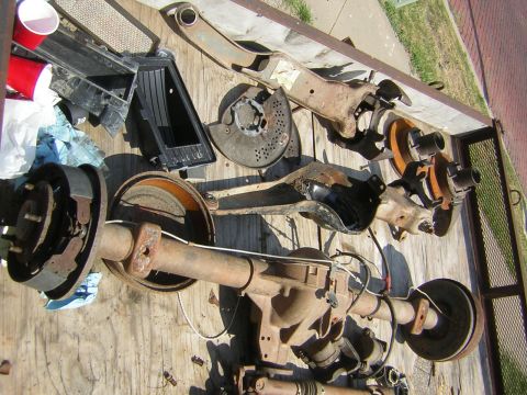 1995 Ford Bronco - Various rusty vehicle parts, including a rear axle, are spread out on a wooden surface.