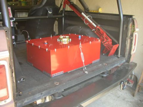 1995 Ford Bronco - A large red auxiliary fuel tank is installed in the cargo area of a vehicle, alongside a roll cage and a high-lift jack.