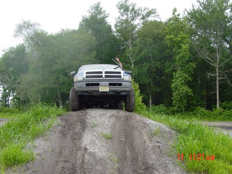 1995 Dodge 1500 - A blue pickup truck is shown from the front, ascending a dirt mound with trees in the background.