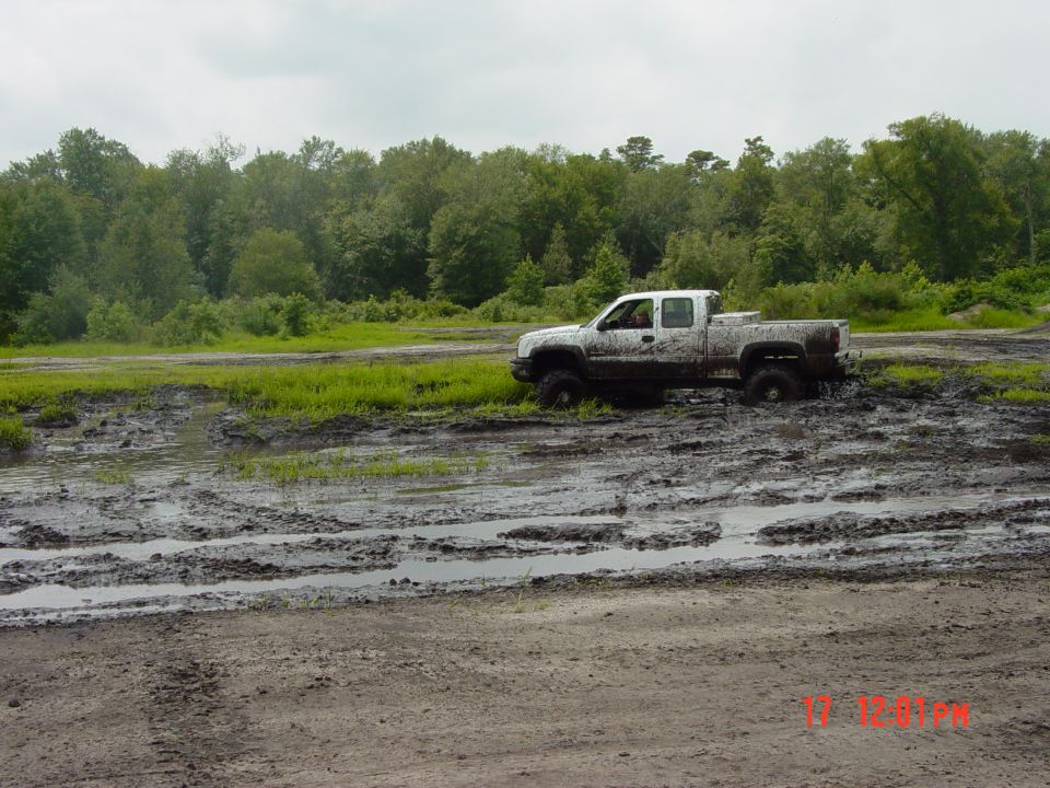 White pickup truck stuck in mud pit with trees in background