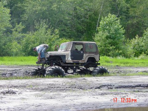 1995 Dodge 1500 - A heavily modified Jeep Wrangler with oversized tires is stuck in the mud while a person works on its front end.