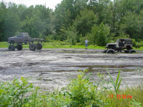 1995 Dodge 1500 - Two heavily modified trucks are stuck in a muddy field, with one appearing to be a tow truck.