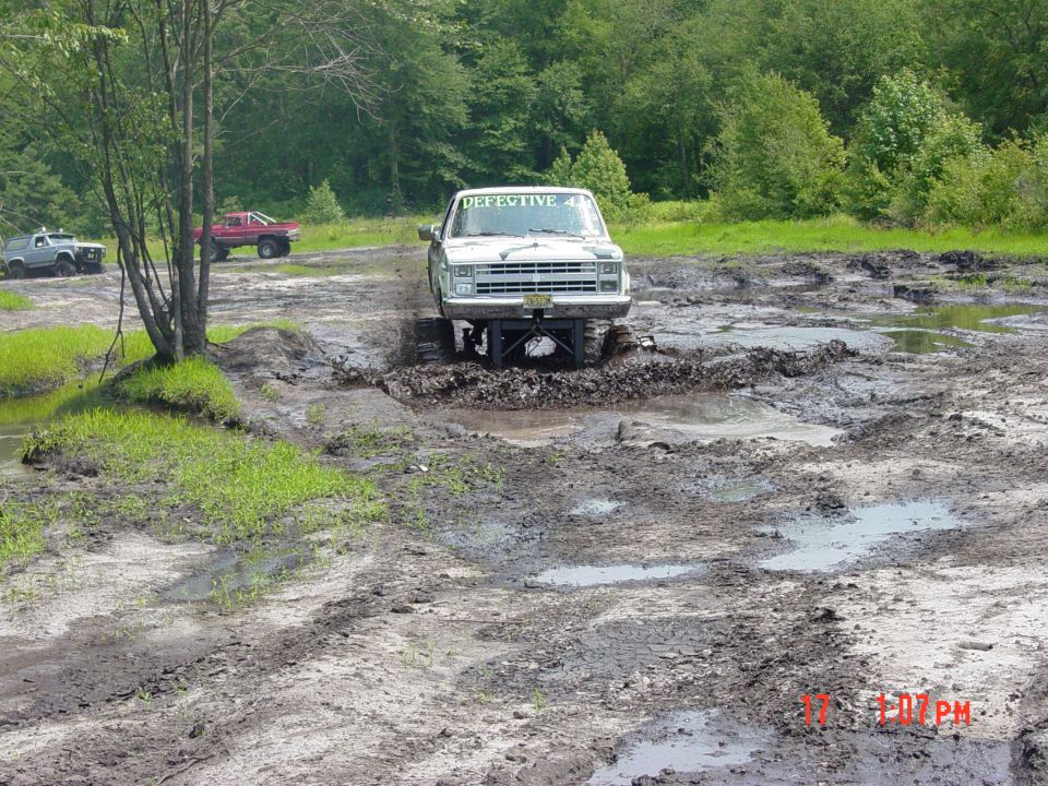 White pickup truck with "DEFECTIVE 4" on windshield stuck in mud