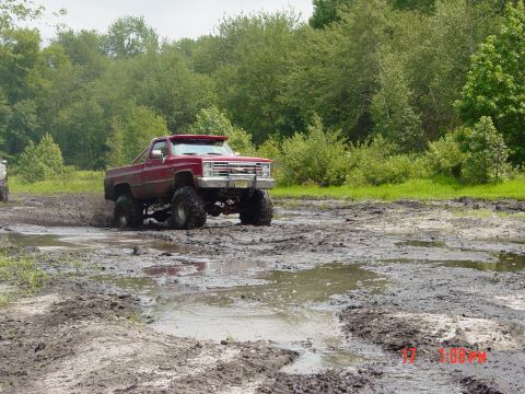 1995 Dodge 1500 - A lifted red pickup truck navigates a muddy off-road course, its large tires designed for challenging terrain.