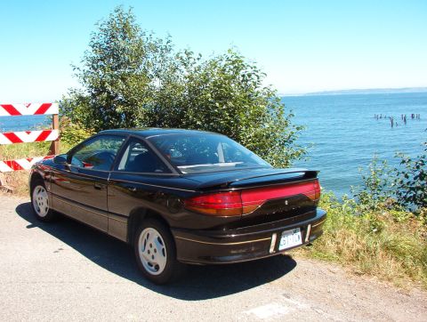 1981 Ford Bronco - 1991 Saturn SC coupe parked near the water with a red and clear taillight bar.