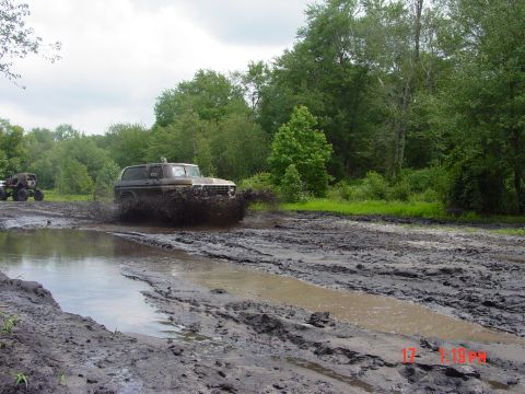1995 Dodge 1500 - An off-road SUV navigates a muddy track, sending mud flying as it drives through a water puddle.
