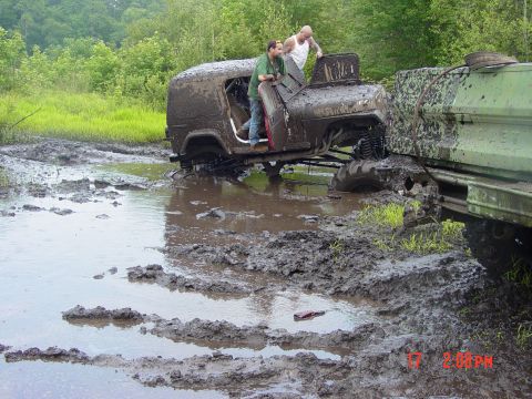 1995 Dodge 1500 - Two heavily mud-covered off-road vehicles are stuck in a muddy field, with two people visible on one of the vehicles.