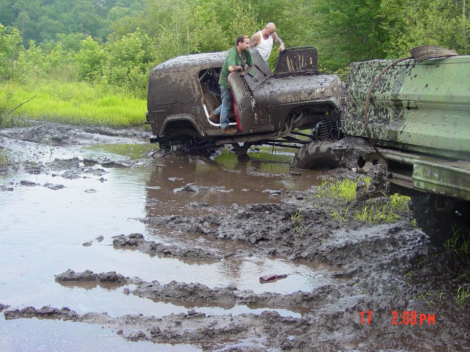 Muddy off-road vehicles stuck in a muddy field with people standing on them