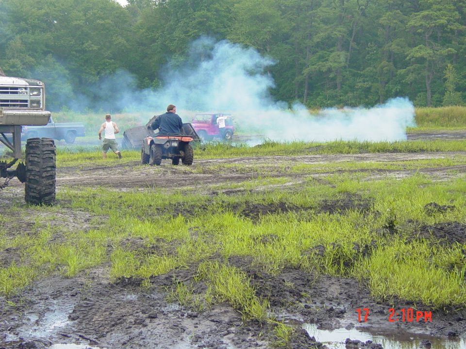 ATV kicking up smoke with people and trucks in muddy field