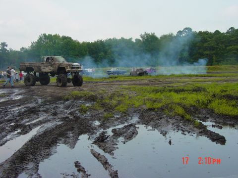 1995 Dodge 1500 - A lifted pickup truck navigates a muddy terrain, with other vehicles and smoke visible in the distance.