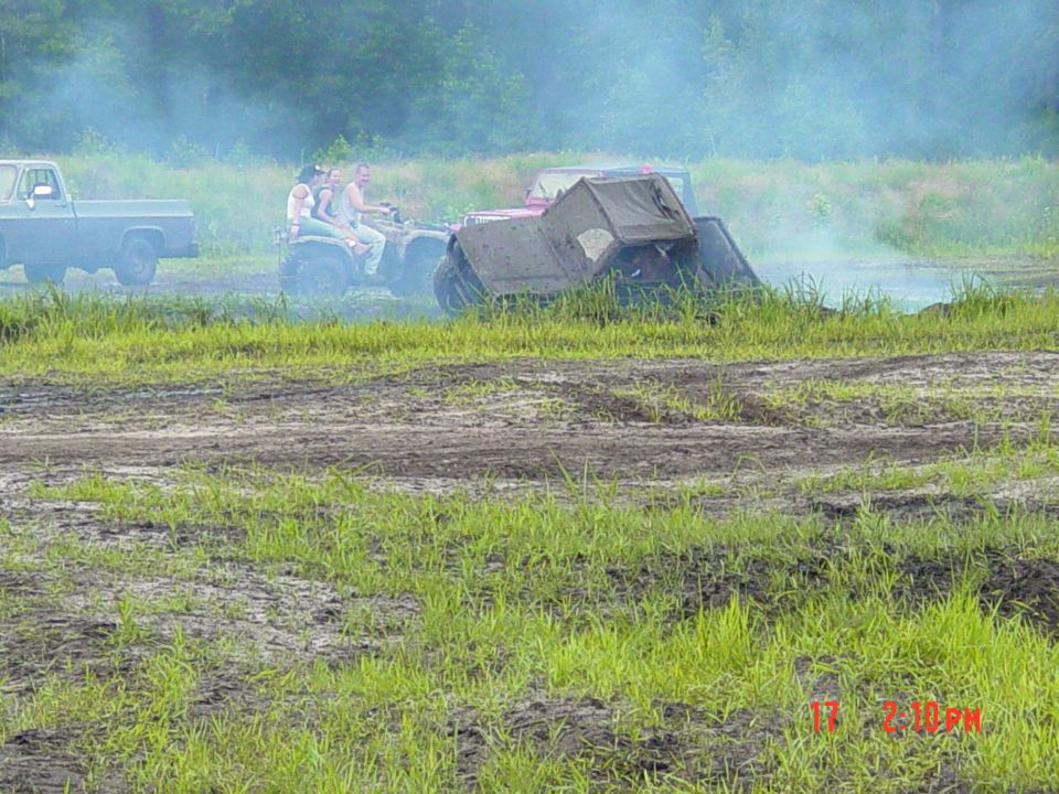 ATV with three people stuck in mud, with a pickup truck nearby
