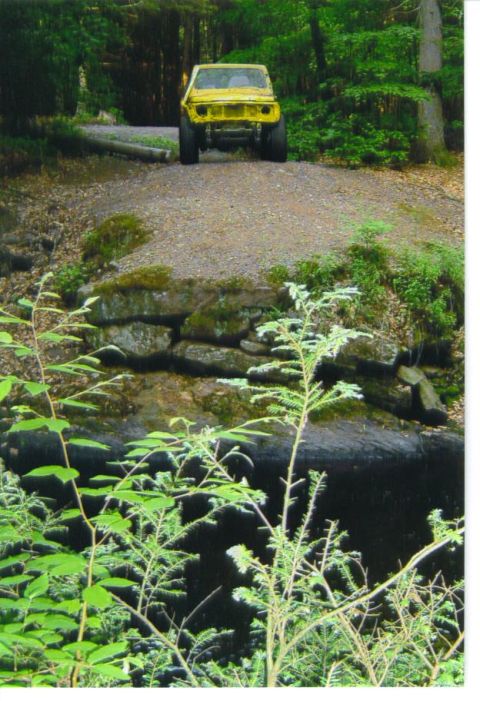 1987 Suzuki Samurai - A yellow off-road vehicle is parked on a gravel path surrounded by trees and foliage.