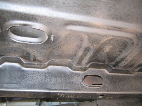 1969 Ford Ranchero - The underside of a vehicle chassis shows stamped metal sections and an oval-shaped opening. Some faint text is visible.