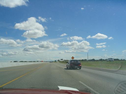 Dark red 1994 Ford Probe driving on a highway, rear view. Another white vehicle is parked on the shoulder