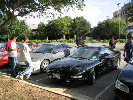 Black 1994 Ford Probe parked next to a gray Ford Probe, with people standing around