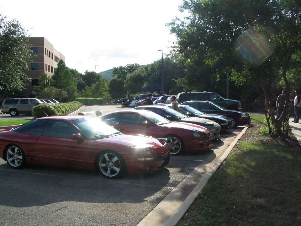 Red coupe parked in a lot with other cars and a building in the background