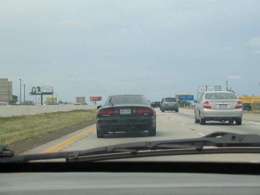 Black sedan from rear, driving on highway. License plate visible