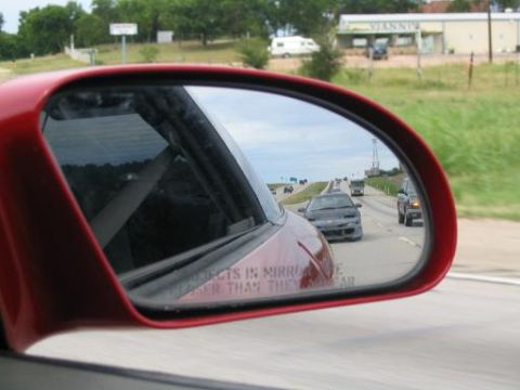 1994 Ford Probe - Highway traffic viewed through a side mirror, with a warning about object proximity.