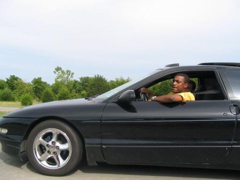 1994 Ford Probe - A man in a yellow shirt drives a black 1994 Ford Probe on a sunny day.