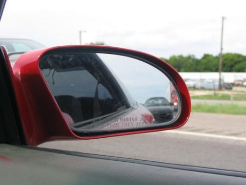 1994 Ford Probe - A red car's side mirror shows a black car in its reflection.