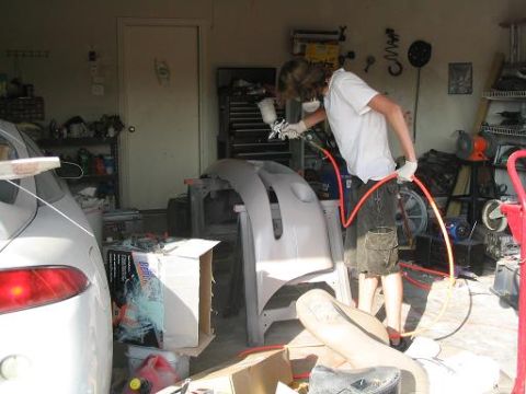 1994 Ford Probe - A person sprays a car bumper in a cluttered garage setting.
