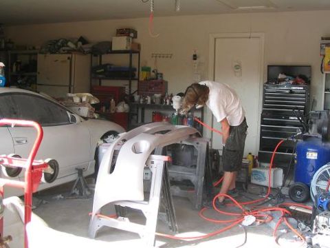 1994 Ford Probe - A person is painting a car bumper in a garage setting, with a white car visible.