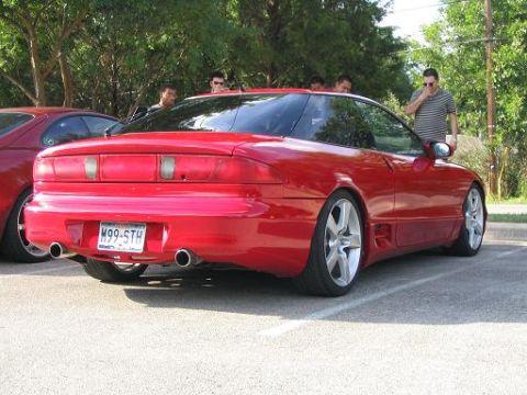 1994 Ford Probe - A red sports coupe is parked in a lot, with another vehicle and several people visible.