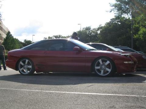 1994 Ford Probe - A red 1994 Ford Probe is parked next to another vehicle, its side profile and custom wheels.