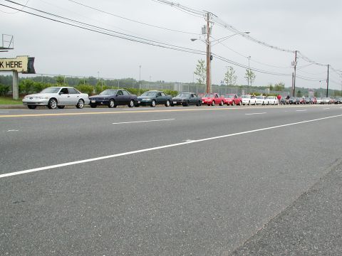 1992 Ford Taurus - A line of cars, including a silver 1992 Ford Taurus, are parked along the side of a road.