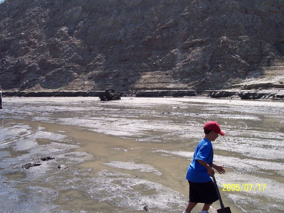 Kid with shovel walks through mud near a truck in a rocky, dry riverbed