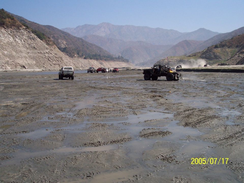 Off-road vehicles in a muddy riverbed with mountains in the background
