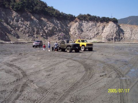 1985 Ford Bronco - Off-road vehicles gathered in a dry lake bed with rocky hills behind them.
