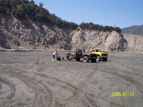 1985 Ford Bronco - Two trucks are parked in a dry, sandy area with a rocky cliff face behind them.