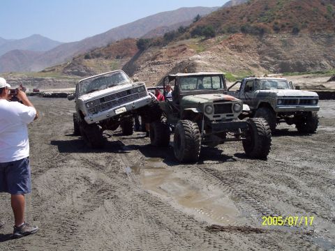 1985 Ford Bronco - Modified trucks navigating a muddy terrain, with one vehicle tilted precariously.
