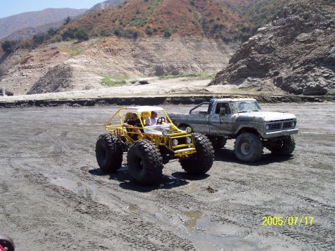 1985 Ford Bronco - A yellow buggy and a lifted pickup truck are parked on a muddy terrain with hills in the background.