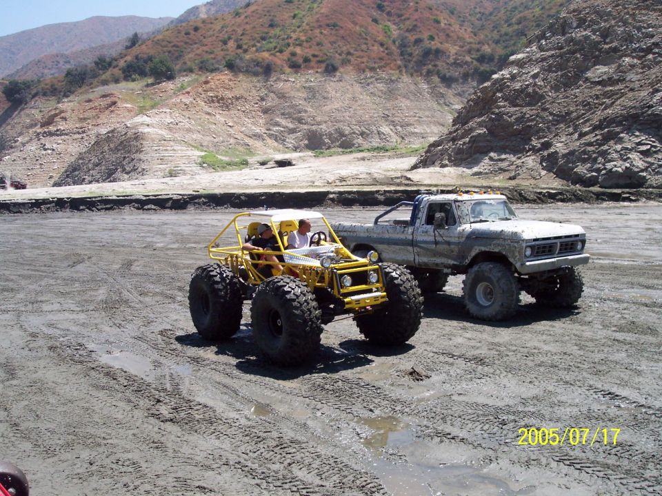 Two off-road vehicles, a yellow buggy and a lifted pickup truck, on a muddy surface