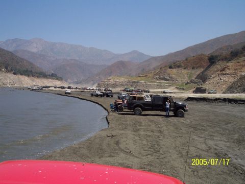 1985 Ford Bronco - Off-road vehicles gathered by a lake on a sunny day, with mountains visible in the distance.
