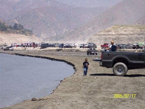 1985 Ford Bronco - A group of people and vehicles are gathered near a body of water on a sunny day.