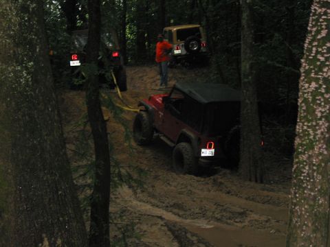 2000 Jeep Grand Cherokee - Multiple Jeeps navigate a challenging muddy off-road trail through a wooded area.