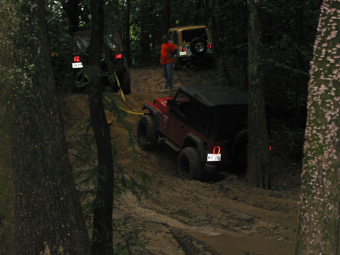 Red Jeep Wrangler on a muddy trail with other vehicles in the background