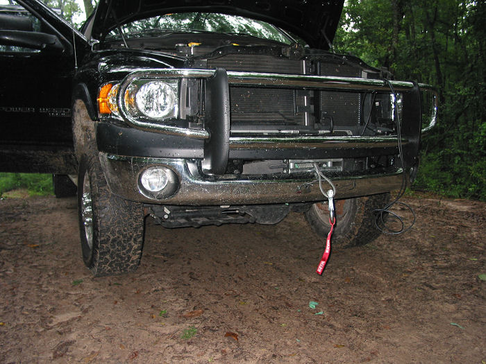 Front view of a black pickup truck with hood open and a chrome bull bar. It's parked on a dirt road