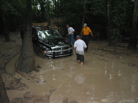 2000 Jeep Grand Cherokee - A black pickup truck is stuck in a muddy wooded area with three men observing.