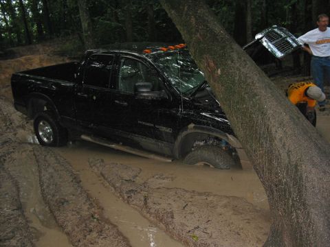 2000 Jeep Grand Cherokee - A black pickup truck is stuck in a muddy off-road trail, with a large tree leaning over its hood.
