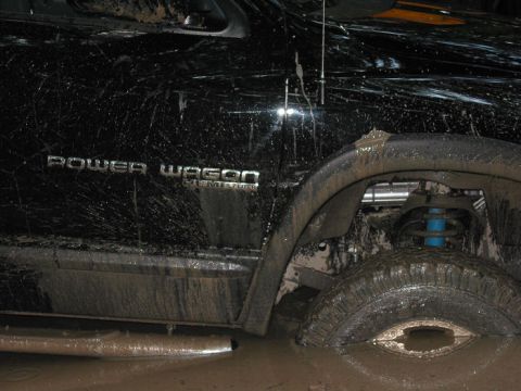 2000 Jeep Grand Cherokee - A black truck, heavily coated in mud, is stuck in a muddy area, with its front wheel submerged.