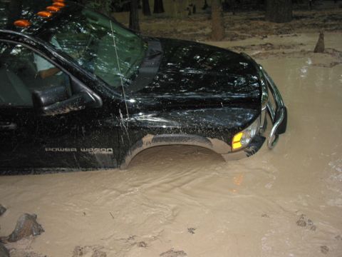 2000 Jeep Grand Cherokee - A black pickup truck, identified as a Power Wagon, is stuck in deep mud, indicating a challenging off-road situation.
