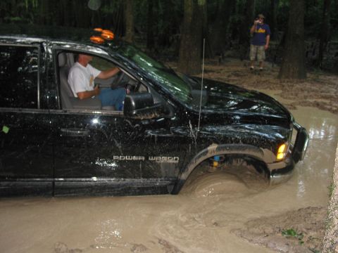 2000 Jeep Grand Cherokee - A black pickup truck navigates through a muddy off-road trail, with one person driving and another observing.