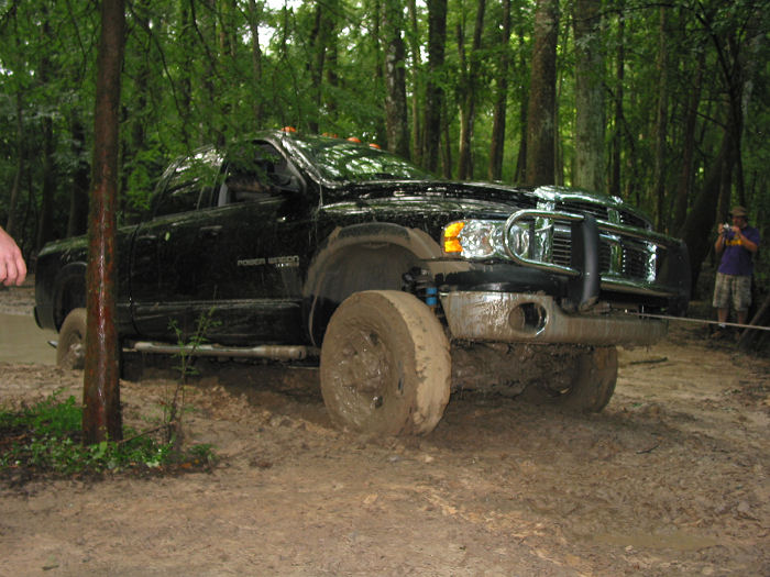 Black Dodge Ram pickup truck stuck in mud, front wheel deep in mud, trees in background