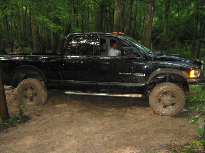 Black pickup truck with 'Power Wagon' badging stuck in muddy terrain with trees in background