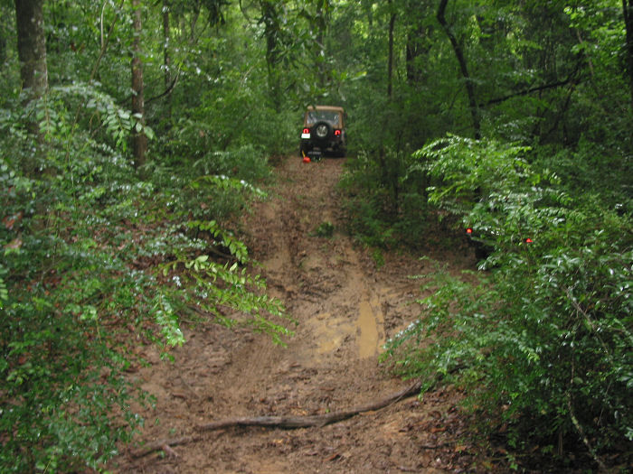 Rear view of a Jeep Wrangler on a muddy trail, with another vehicle partially visible to the right