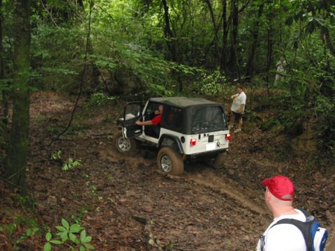 2000 Jeep Grand Cherokee - A white Jeep Wrangler navigates a muddy off-road trail surrounded by dense trees.